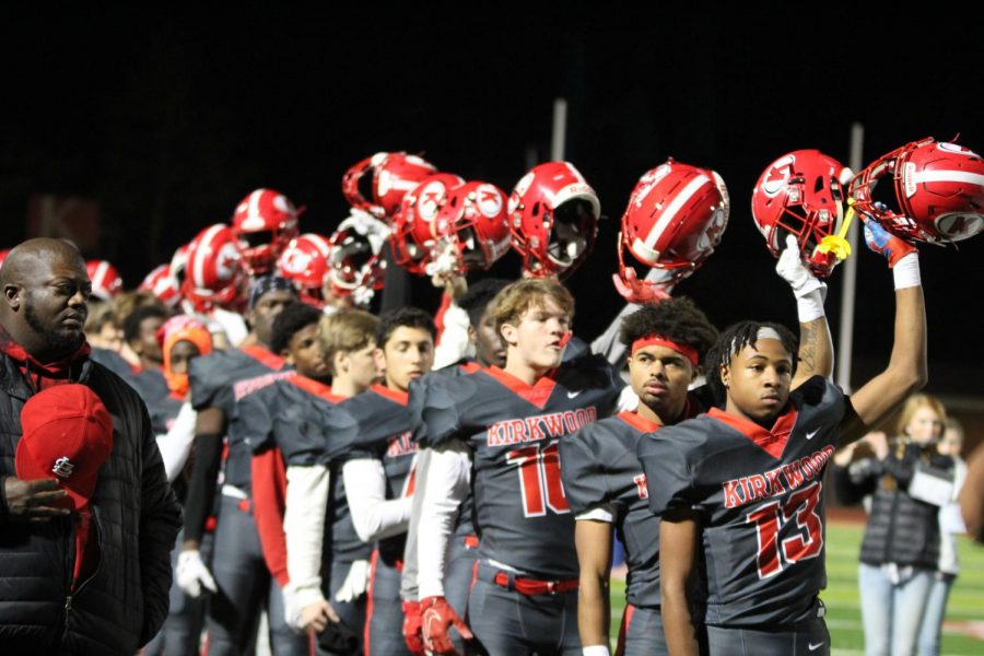 The football players raise their helmets for the national anthem.