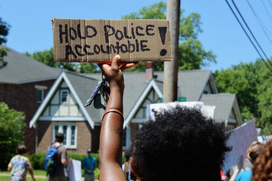 A young woman holds up a cardboard sign as she walks with the protest. 