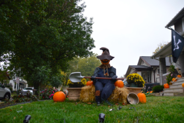 A pumpkin man sits on a barrel of hay with a shovel.