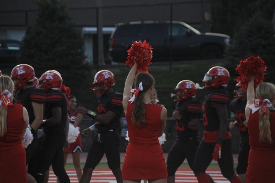 Kirkwood cheerleaders stand forming a path as the varsity football team runs through, starting off the game.