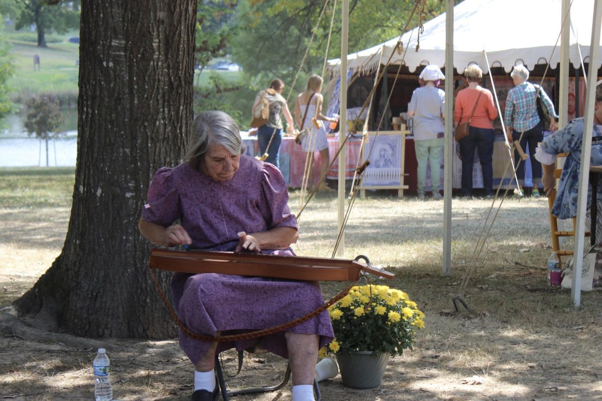 Volunteer plays an instrument in the folk life area of the Greentree festival.