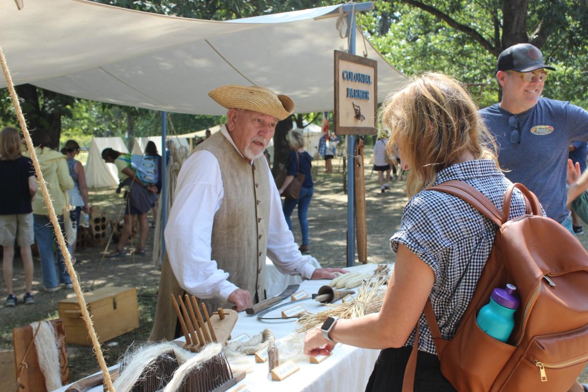 A man explains various colonial farming equipment at a display table.
