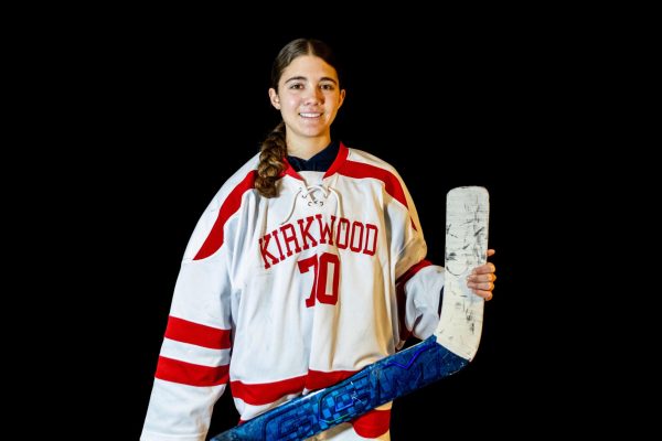 Ava Whaley, junior, clad in her Kirkwood Hockey jersey and smiling with a hockey stick in hand.